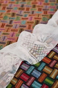 Detail view of colorful geometric woven fabric with white floral lace trim and texture