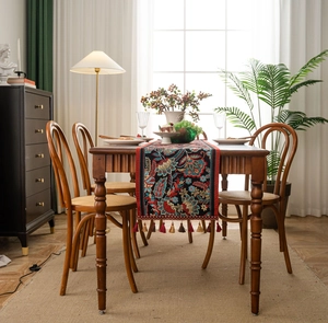 Detailed jacquard floral table runner with red and brown tassel fringe on a wooden table