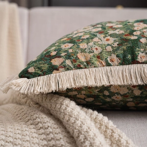 Close-up of dark green jacquard pillow fabric with floral patterns and creamy white fringe