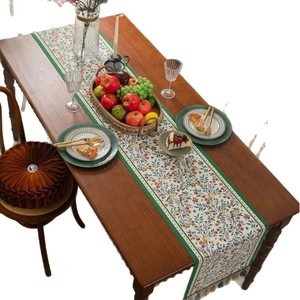 Floral table runner with green trim and tassels on a wooden dining table setup