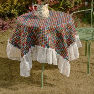 Colorful woven round tablecloth with white lace edges on a garden table setup