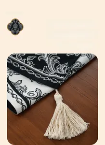 Detail of black and white jacquard table runner with handmade tassels on wooden surface