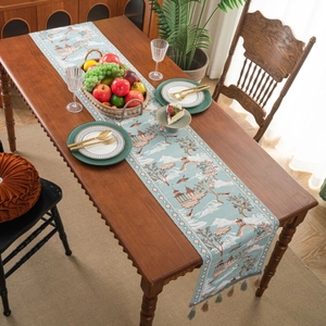 Blue Chinoiserie table runner with landscape painting and elegant fringe on a wooden table