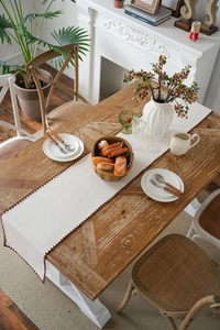 Detail of cream table runner featuring elegant burgundy scalloped embroidery on wood table
