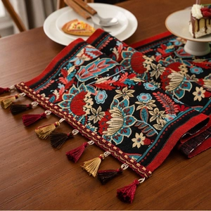 Ethnic jacquard table runner with red floral patterns and tassels on dark wood table
