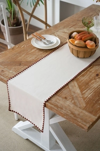 Detail of cream table runner with red scalloped embroidery on rustic wooden table