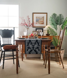 Detail of black table runner with classical scroll patterns and cream-colored tassels