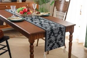 Elegant black table runner with white jacquard floral patterns and cream tassels on wood table