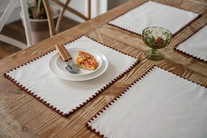 Detail of beige table runner with brown scalloped embroidery on a rustic wooden table