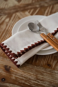 Detail of a beige linen napkin with dark brown scalloped edges and rustic wood background