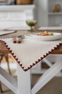 Detail of cream table runner with rustic reddish-brown triangle embroidery on wooden table