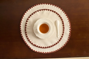 Macro detail of round cotton linen placemat with contrast embroidery on wooden table