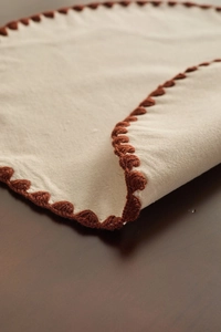 Close-up of cream table runner with rustic terracotta crochet lace edges on wooden table