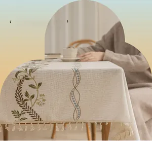 Detailed view of linen tablecloth featuring vine embroidery and elegant beige tassels