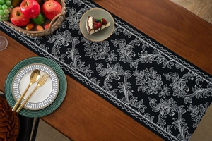 Detail of black and white jacquard table runner with vine floral pattern on wooden table