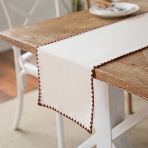 Beige American country style table runner with brown scalloped trim on wood table
