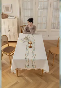 Detail of cream cotton linen tablecloth with green floral embroidery and white pompom fringe