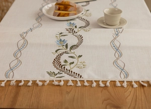 Macro detail of beige cotton linen table runner with blue floral embroidery and white tassels