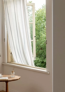 Detail of white cotton linen curtain with blue vertical waves and white fringe tassels
