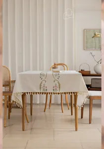 Detailed view of beige linen tablecloth with floral embroidery and tassel fringe