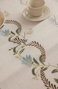 Close-up of beige linen tablecloth featuring intricate floral embroidery and tassel detail