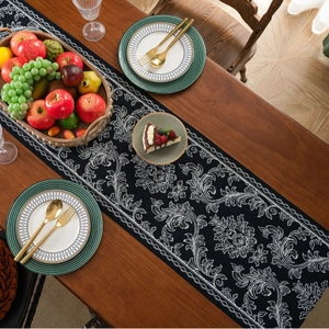 Elegant black table runner with white Baroque floral embroidery on a dark wooden table