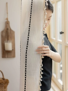 Détail du rideau bohème montrant la broderie noire en V et les pompons en coton doux