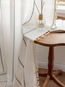Close-up of linen curtain with blue leaf embroidery and elegant white pompom fringe