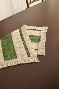 Detail of woven table runner with green stripes, geometric texture and fringe accents