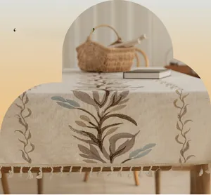 Detailed embroidery of leaf patterns on beige linen tablecloth with elegant tassels