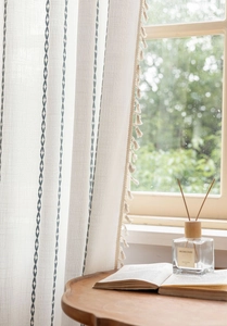 Detail of cream linen curtain with blue embroidered stripes and decorative tassels