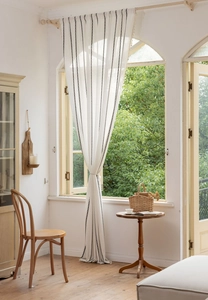 Détail du rideau en coton blanc avec lignes noires verticales et pompons décoratifs