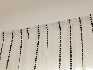 Détail d'un rideau en lin crème avec des rayures à motifs de feuilles noires et drapé élégant