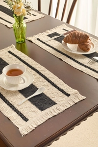 Detailed view of woven black and white striped placemat with tassels on a wooden table