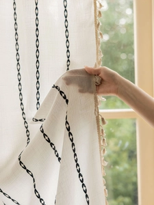 Gros plan d'un rideau beige semi-transparent en lin avec motifs géométriques et glands