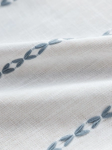 Macro detail of blue leaf embroidery on grey linen fabric for rustic style curtains
