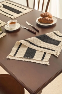 Detail of woven table mat with black and beige stripes and decorative fringe edges