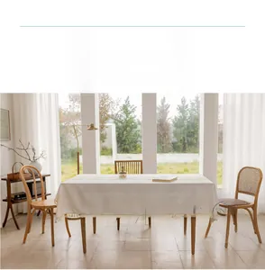 Detail of light beige cotton linen tablecloth with ivory tassels on a rectangular table
