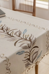 Close-up of linen tablecloth with leaf embroidery and decorative fringe tassels