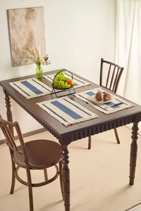 Close-up of woven striped placemats with tassels on a rustic dark wood dining table