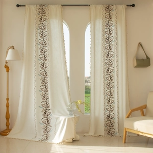 Detailed close-up of beige linen curtains with leaf embroidery and bohemian tassels