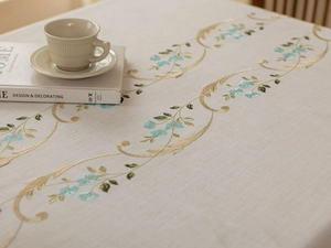 Detail of floral embroidery on beige linen tablecloth with intricate gold leaf patterns