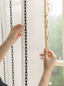Détail du rideau en lin avec broderie géométrique noire et bordure à pompons
