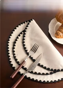 Close-up of beige cotton linen placemat with black pompom fringe on a wooden table