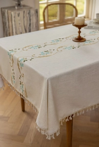 Close-up of elegant floral embroidery and fringe detail on linen dining tablecloth
