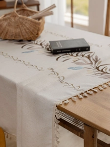Close-up of linen tablecloth with botanical leaf embroidery and fringe tassels