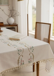 Detailed close-up of beige cotton linen tablecloth with floral embroidery and tassels