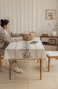 Close-up of beige cotton linen tablecloth featuring leaf embroidery and fringe edges
