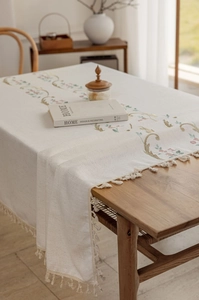 Close-up of elegant floral embroidery and tassel fringe on beige cotton linen tablecloth