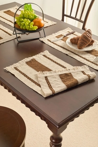 Detail of Nordic woven place mat with brown stripes and decorative fringe on wood table